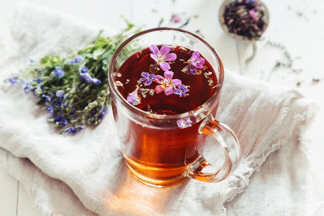 A glass mug of pale herbal infusion beside loose dried flowers