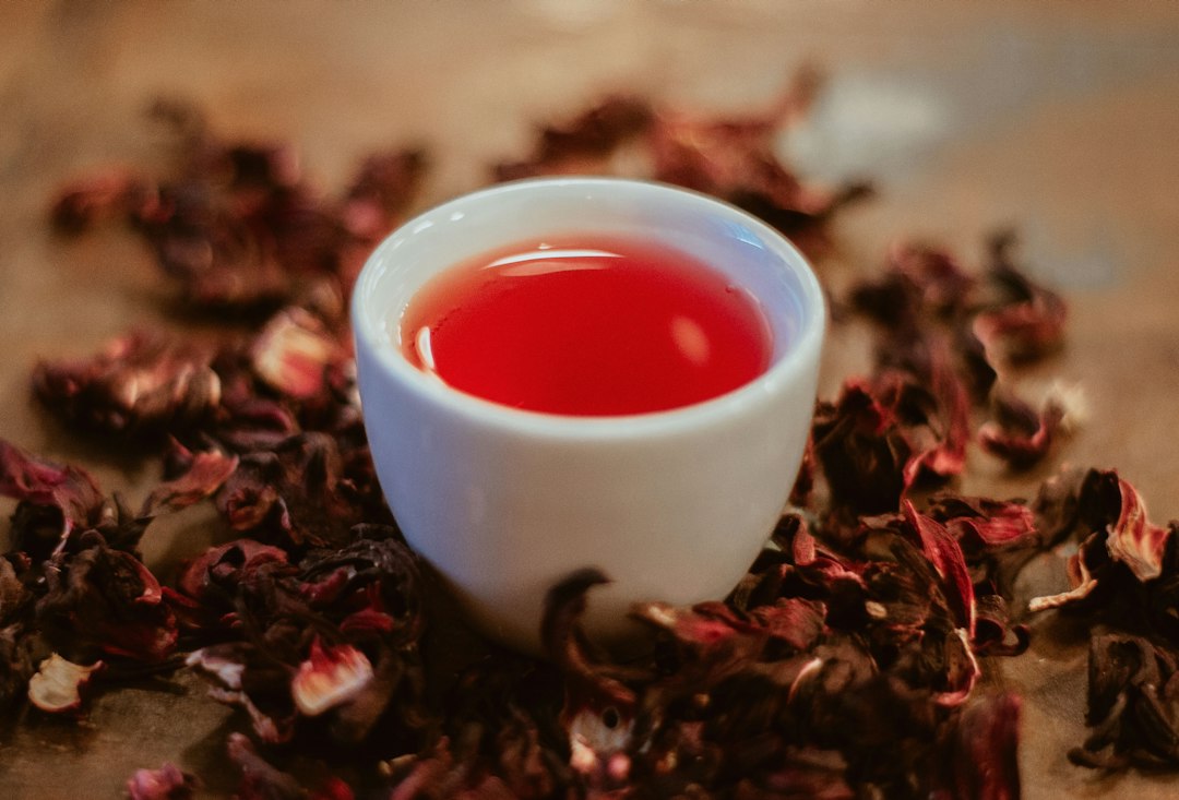 Cup of red hibiscus tea surrounded by dried roselle calyces