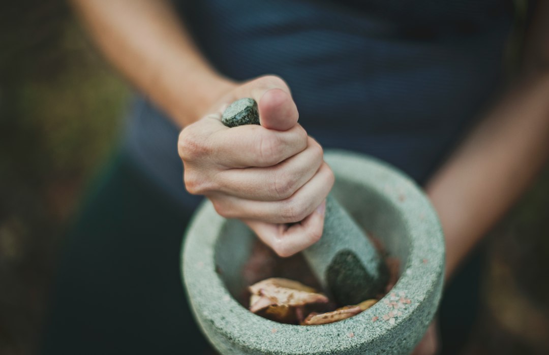 Dried herbs being ground with a mortar and pestle before extraction