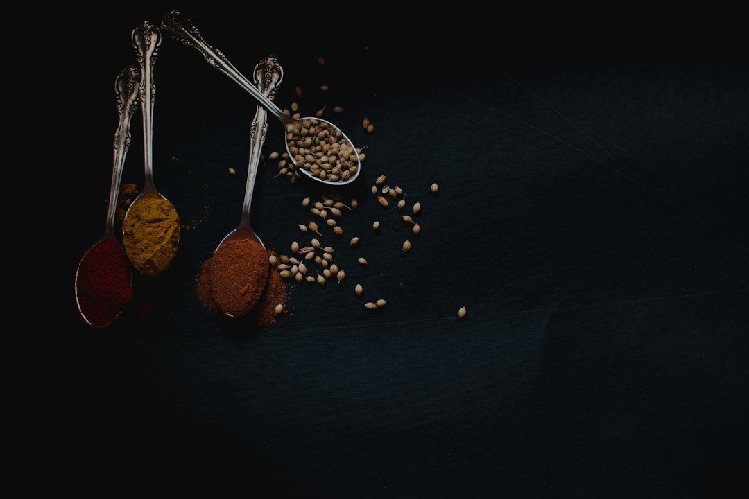 Spoons of ground spices and whole seeds on a dark table